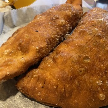 Culantro - Empanadas - Two fried empanadas with golden, crispy crusts are placed on parchment paper. The empanadas have a textured surface with small bubbles and a slightly oily appearance. The background suggests a restaurant setting, possibly at Culantro in Ferndale, MI, known for Peruvian cuisine. - Peruvian Near Me - Ferndale, Michigan