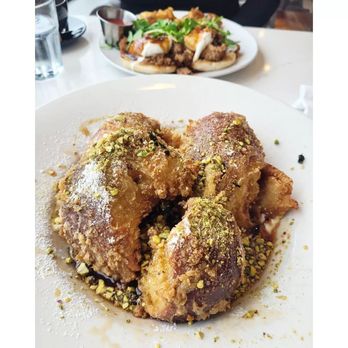 HeadQuarters - French Toast - A fried dessert garnished with chopped pistachios and powdered sugar, served on a white plate, with another dish in the background. - Cafes Near Me - Ottawa, Ontario