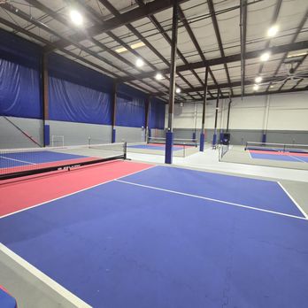Pickleball4All - A spacious indoor pickleball facility featuring multiple courts with blue and red surfaces, high ceilings, and overhead lighting. - Pickleball Near Me - Glenview, Illinois