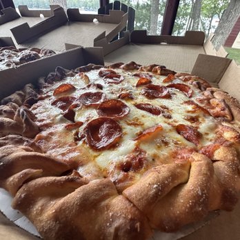 The Dock - Crispy pepperoni - that crust tho! - A pepperoni pizza with a thick, golden-brown crust and melted cheese topped with slices of pepperoni is shown in an open pizza box. The pizza is placed on a table near large windows, revealing a view of trees and a lake outside. The setting suggests a casual dining environment, possibly at a lakeside business or restaurant. - Pizza Near Me - Hayward, Wisconsin