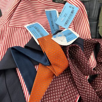ACTS Thrift Store - 1/2 off on blue tags this week!!! - Several clothing items, including a red and white striped shirt, dark-colored ties, and patterned fabric, are arranged on a surface. The items have blue price tags attached, indicating prices such as $2.99 and $5.99. The tags also display barcodes and store information. The clothing appears to be new or used items for sale, possibly in a thrift or retail store setting. - Thrift Stores Near Me - Pasadena, California
