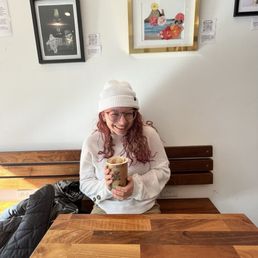 Red headed girl holding up a beautifully crafted latte featuring local art on the wall Red headed girl holding up a beautifully crafted latte featuring local art on the wall