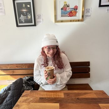 Elementary Coffee - Red headed girl holding up a beautifully crafted latte featuring local art on the wall - Coffee Roasteries Near Me - Harrisburg, Pennsylvania Elementary Coffee - Red headed girl holding up a beautifully crafted latte featuring local art on the wall - Coffee Roasteries Near Me - Harrisburg, Pennsylvania