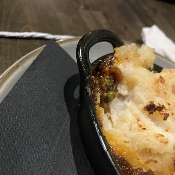 Slainte of Peekskill - Shepherd's pie - A shepherd's pie served in a small black dish, topped with mashed potatoes and baked until golden brown, on a wooden table. - Irish Pub Near Me - Peekskill, New York