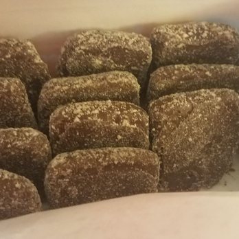 Candy Kitchen Shoppes - a box of donuts - A box contains several chocolate-covered treats, each dusted with powdered sugar. The treats are arranged in rows inside a box, with some overlapping slightly. The image focuses on the confections, which appear to be a sweet snack or dessert item. - Candy Stores Near Me - Bethany Beach, Delaware