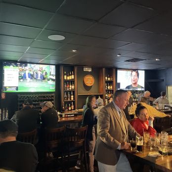 The Tap - Inside Vibe - A busy bar or pub with patrons seated at tables and the bar, two TVs on the wall, and a dark ceiling. - Pubs Near Me - Cumberland, Rhode Island