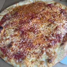 A cheese pizza with a slightly uneven, golden-brown crust is displayed inside a cardboard pizza box. The pizza is topped with melted cheese and tomato sauce, with some areas showing more cheese coverage than others. The pizza appears to be freshly baked, with some darker spots on the crust indicating charring from baking.