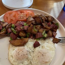 Corned beef hash with over easy eggs and an extra side of sliced tomatoes.