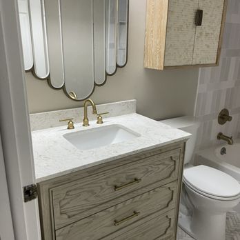Omega Contractors - a bathroom with a sink, toilet, and mirror - Flooring Near Me Omega Contractors - a bathroom with a sink, toilet, and mirror - Flooring Near Me