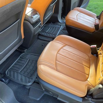 Pristine Detailing Pros - The image depicts the back seats of a vehicle with tan leather upholstery, black floor mats, and part of the front seats and door panels. - Auto Detailing Near Me