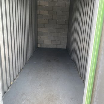 Extra Space Storage - storage unit 5x15 - An empty storage unit features metal walls with vertical ridges, a concrete floor with some dirt marks, and a brick wall at the back. The ceiling has a metallic vent or duct, and the space appears clean and unused. - Self Storage Near Me - Boca Raton, Florida