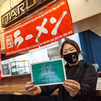 Naruto Mampuku - a woman wearing a face mask holding a sign - Ramen Near Me - Albuquerque, New Mexico