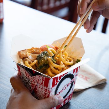 Wok Box - a person holding chopsticks over a bowl of noodles - Asian Fusion Near Me - Lloydminster, Alberta