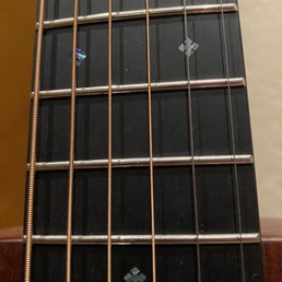 A guitar neck with metal strings, fret markers, and a black fretboard is shown in close-up, highlighting the details of the instrument.