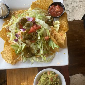 Martha's Exchange - Nachos - A serving of nachos with shredded lettuce, jalapeños, diced tomatoes, and onions, accompanied by salsa and guacamole, on a white plate. - New American Near Me - Nashua, New Hampshire
