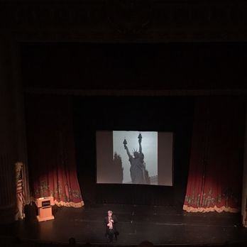 The Capitol Theatre - a woman standing on stage in front of a projection of the statue of liberty - Performing Arts Near Me - Yakima, Washington The Capitol Theatre - a woman standing on stage in front of a projection of the statue of liberty - Performing Arts Near Me - Yakima, Washington