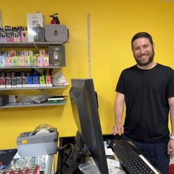 Trippy Smoke Shop - The proprietor in front of the bright yellow, cheery wall and a selection of vibey stuff for chillin' ....