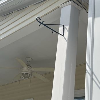 Pro Quality - Plant hanger times 2 - A black metal plant hanger is mounted on a white porch column outside a house, with a ceiling fan and window visible in the background. - Handyman Near Me