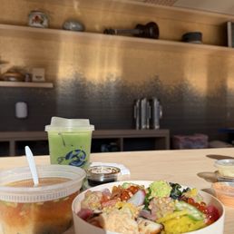 Premium Shaken Matcha - A meal setup includes a bowl of chirashi sushi with various toppings, a container of miso soup, and a green matcha drink in a plastic cup, all on a wooden table.