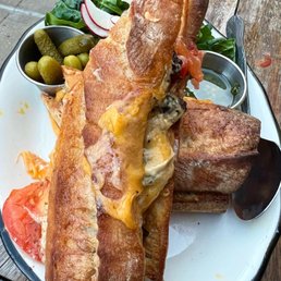 Filet mignon Sandwich Bauru - Fried fish fillets served with sides of pickles, sliced tomatoes, and fresh greens on a white plate.