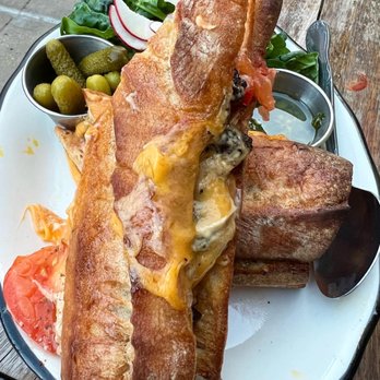 Beco - Filet mignon Sandwich Bauru - Fried fish fillets served with sides of pickles, sliced tomatoes, and fresh greens on a white plate. - Brazilian Near Me - Brooklyn, New York