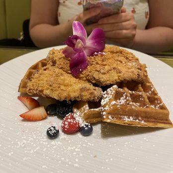 Giardino - Chicken and waffles - A plate featuring fried chicken on a waffle, decorated with an orchid flower and fresh berries, served with powdered sugar. - Juice Bars & Smoothies Near Me - Everett, Massachusetts