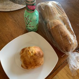 Sausage and Cheese Calzone, loaf of bread, and Arizona green Tea - A baked pastry on a white plate, a loaf of sliced bread in a plastic bag, a bottled green tea, and a croissant on a wooden table.