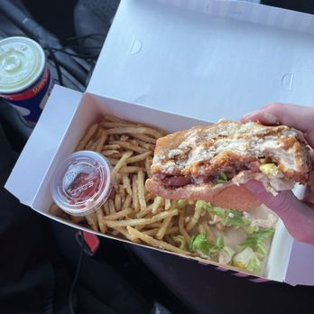 Stripes Burrito - Worlds famous chicken sandwich  French fries  lemonade - A hand holds a chicken sandwich with lettuce, tomato, and sauce, over a box of fries, with a small container of ketchup, in a vehicle. - New Mexican Cuisine Near Me - Rio Rancho, New Mexico