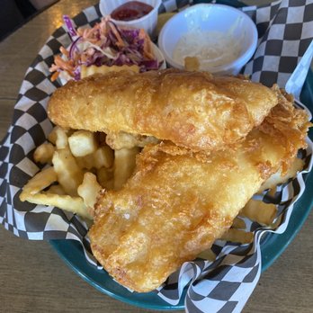 The Kosmos - Fish and chips!! Yum! - A basket containing two pieces of battered fish, French fries, coleslaw, ketchup, and tartar sauce, served on checkered paper. - Bars Near Me - Albuquerque, New Mexico