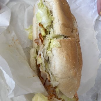 Carmella's Market - Buffalo chix - A sandwich with shredded lettuce and sliced deli meat in a hoagie bun, placed on white paper, with some lettuce pieces outside. - Cheese Shops Near Me - Boston, Massachusetts