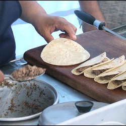 Chapa - From a warm pot, wife spoons barbacoa on a toasted tortilla.  Tacos to the right are awaiting onion and cilantro for garnish.