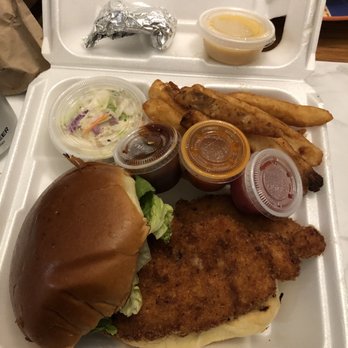 The Pit - SOUTHERN FRIED CHICKEN SANDWICH - A foam take-out container holds fried fish, potato wedges, a sandwich with lettuce, and multiple small containers of sauces, with a small cup of soup or sauce on the lid. - Barbeque Near Me - Edgewater, New Jersey