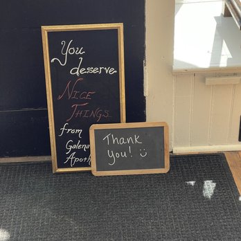 Galena Apothecary - A chalkboard sign with a handwritten message saying 'Thank you! :)' is positioned on the floor next to a framed sign that reads 'You deserve NICE THINGS... from Galena Apothecary.' The signs are placed on a dark carpeted floor near a door with a window, allowing natural light to illuminate the area. The setting appears to be the entrance of Galena Apothecary, a boutique offering personal care products. - Cosmetics & Beauty Supply Near Me - Galena, Illinois