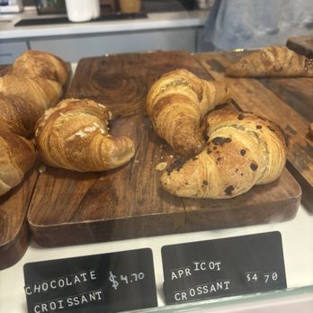Lore’s Cafe - Assorted croissants and croissant-shaped pastries are arranged on a wooden board at a bakery, with price tags indicating $4.70. - Cafes Near Me - Beacon, New York