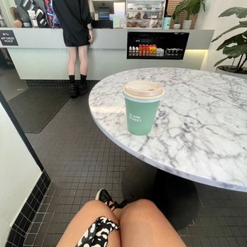 Blank Street Coffee - a woman sitting at a table with a cup of coffee - Coffee & Tea Near Me - New York, New York Blank Street Coffee - a woman sitting at a table with a cup of coffee - Coffee & Tea Near Me - New York, New York