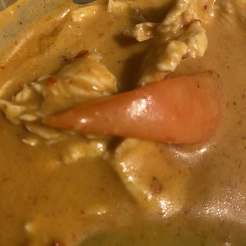 Thai Kitchen - The image shows a close-up of a bowl containing Thai curry with chicken pieces and a large piece of carrot. The curry has a thick, creamy, orange-colored sauce with visible spices and herbs. The dish appears to be served in a restaurant setting, emphasizing traditional Thai flavors and ingredients. - Thai Near Me - Independence, Missouri