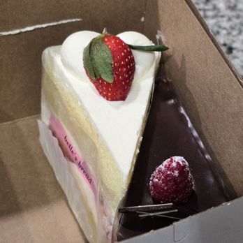 Belle's Bread - Strawberry and Chocolate cake - The image shows a bakery box with two slices of cake. One is a strawberry and cream cake with a fresh strawberry on top, decorated with white frosting and a pink label. The other is a chocolate cake with a dusted raspberry inside, featuring a glossy chocolate surface and a single raspberry. The cakes are arranged side by side inside the box, which is partially open, revealing the desserts inside. - Bakeries Near Me - Columbus, Ohio