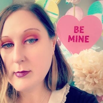 Kdulche Cafe - I look a little moody in this photo hahaha but again you could pose and take a selfie with many things in here - A woman with makeup and a necklace poses for a selfie in front of Valentine's Day decorations, including signs that say 'CANDY' and 'BE MINE.' - Coffee & Tea Near Me - Lansing, Illinois