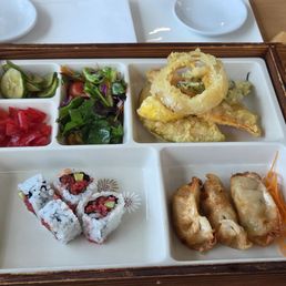 Bento box with veg tempura and dipping sauce, veggie gyoza, plant based spicy tuna rolls, salad, and pickled veggies