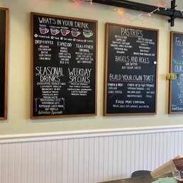the menus on the wall - Two blackboards list drink options, seasonal specials, and pastry selections in a cafe setting, with a string of colorful lights above.