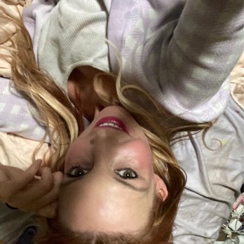 Ulta Beauty - A woman with red hair and makeup is lying on a bed, holding a phone for a selfie, with a relaxed expression. - Cosmetics & Beauty Supply Near Me - Hoffman Estates, Illinois