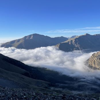 Mount Massive - High mountain peaks rise above a thick layer of clouds, with a clear blue sky overhead, in a scenic mountain landscape. - Hiking Near Me - Leadville, Colorado