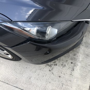 Fixbodycar - Before - The image shows the front right corner of a black vehicle with visible damage to the bumper and headlight area, parked on a concrete surface. - Body Shops Near Me