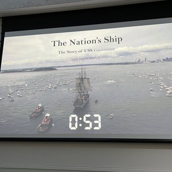 USS Constitution Museum - A projection screen shows details about USS Constitution, including a maritime scene with boats and a historic ship, with a countdown timer. - Museums Near Me - Boston, Massachusetts