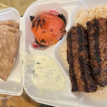 Elia - Adana kebab - A foam takeout container holds grilled meat on rice, a roasted tomato, flatbread, and a creamy sauce, representing Middle Eastern cuisine. - Turkish Near Me - Chicago, Illinois