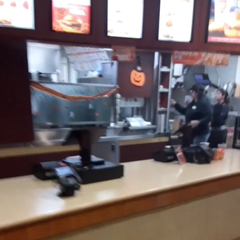 Arby's - The photo depicts the counter area of a fast-food restaurant, with two employees working behind the counter. Digital menu boards are displayed above, showing various food options. Halloween decorations, including a pumpkin face, are visible on the wall. The counter has cash registers and some items placed on it, with a blurred background indicating the kitchen area. - Fast Food Near Me - Tomah, Wisconsin