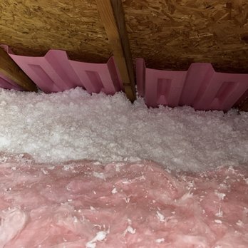 EET Insulation - Post install pics. - The image shows pink foam board insulation installed between wooden wall studs in a construction or renovation setting. The insulation is placed behind a wooden frame, with pink foam backing visible at the bottom of the wall cavity. The floor area is covered with loose pink fiberglass insulation material, indicating ongoing insulation work. - Insulation Installation Near Me