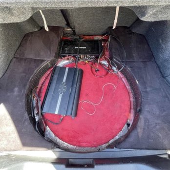 North County Mobile Electronics - Before: how the amps were set up the back, wiring all over the place - Car trunk with audio system components, including an amplifier and wiring, installed on a red circular platform. - Car Stereo Installation Near Me - Oceanside, California