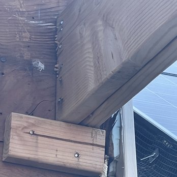 Prehoda Builders - The photo depicts a close-up view of wooden beams and framing components, including a large horizontal beam and a smaller block, fastened with screws. The background shows additional wood and construction materials, indicating an ongoing building or renovation process. The image emphasizes structural elements and hardware used in carpentry or home improvement projects. - General Contractors Near Me