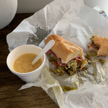 Poor Boy 2 - Chicken and rice soup with half of a 10' poor boy sub - A partially eaten sandwich with ham, lettuce, and pickles on a sesame seed bun, accompanied by a cup of clear soup with rice, on a wooden surface. - Fast Food Near Me - Wheaton, Illinois